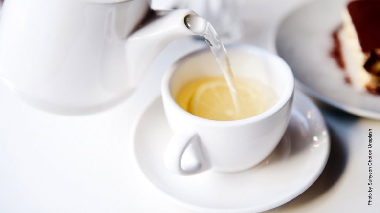 Aus einer Teekanne wird Tee in eine Tasse eingeschenkt