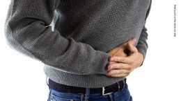 Ein Mann im grauen Pullover at Magenschmerzen hält sich den Bauch