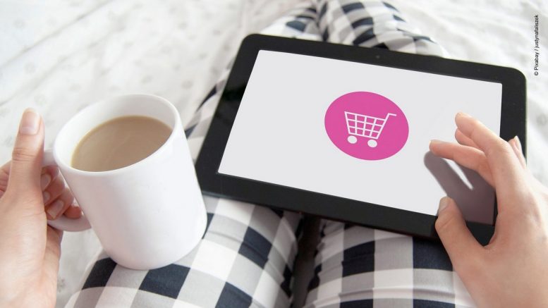 Frau mit Kaffeetasse und Tablet mit Shopping Symbol