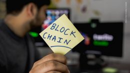 Mann hält Post It mit Blockchain Schriftzug hoch