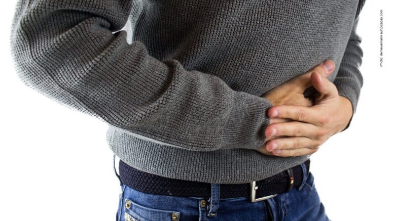 Essstörungen - Mann im grauen Pullover und Jeans hat Bauchschmerzen und hält sich den Bauch
