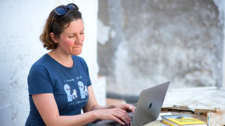 Frau im blauen T-Shirt sitzt im Urlaub am Laptop macht Workation