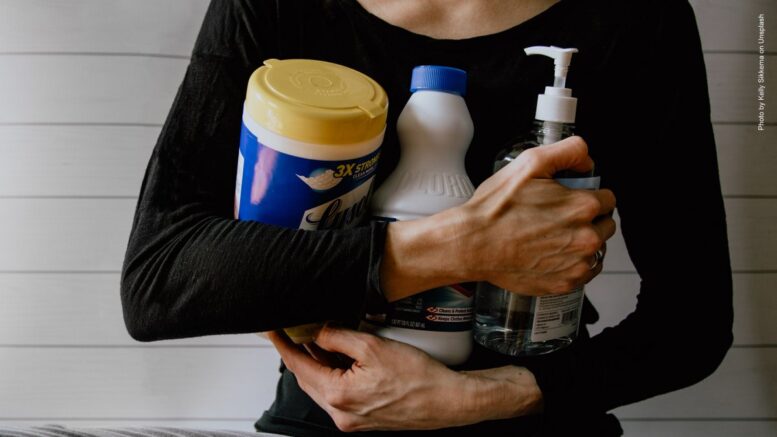 Frau im schwarzen Top hat Desinfektions- und Reinigungsmittel im Arm