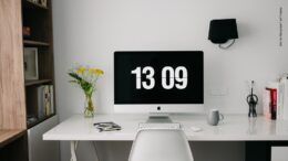 Auch im Home Office muss die Arbeitszeit erfasst werden. Homeoffice Arbeitsplatz mit Uhrzeit auf dem Bildschirm