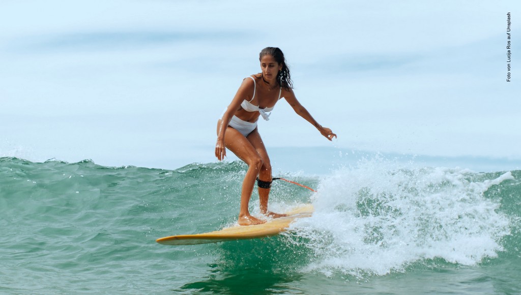 Frau im weißen Bikini auf einem Surfwetter und grün schimmernden Wasser